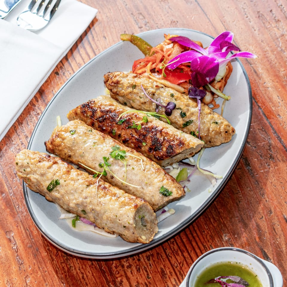 Five grilled seekh kebabs on a platter with pickled vegetables and a purple orchid.