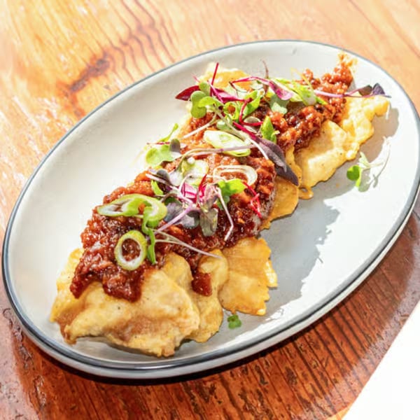 Crispy fried wontons topped with a savory brown sauce, green onions, and microgreens on a white plate.