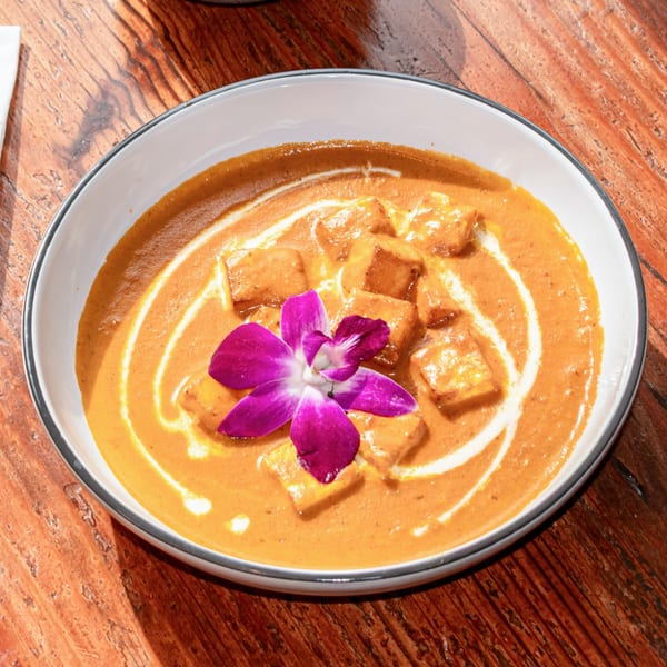Paneer butter masala, garnished with a purple orchid, served in a white bowl on a wooden table.