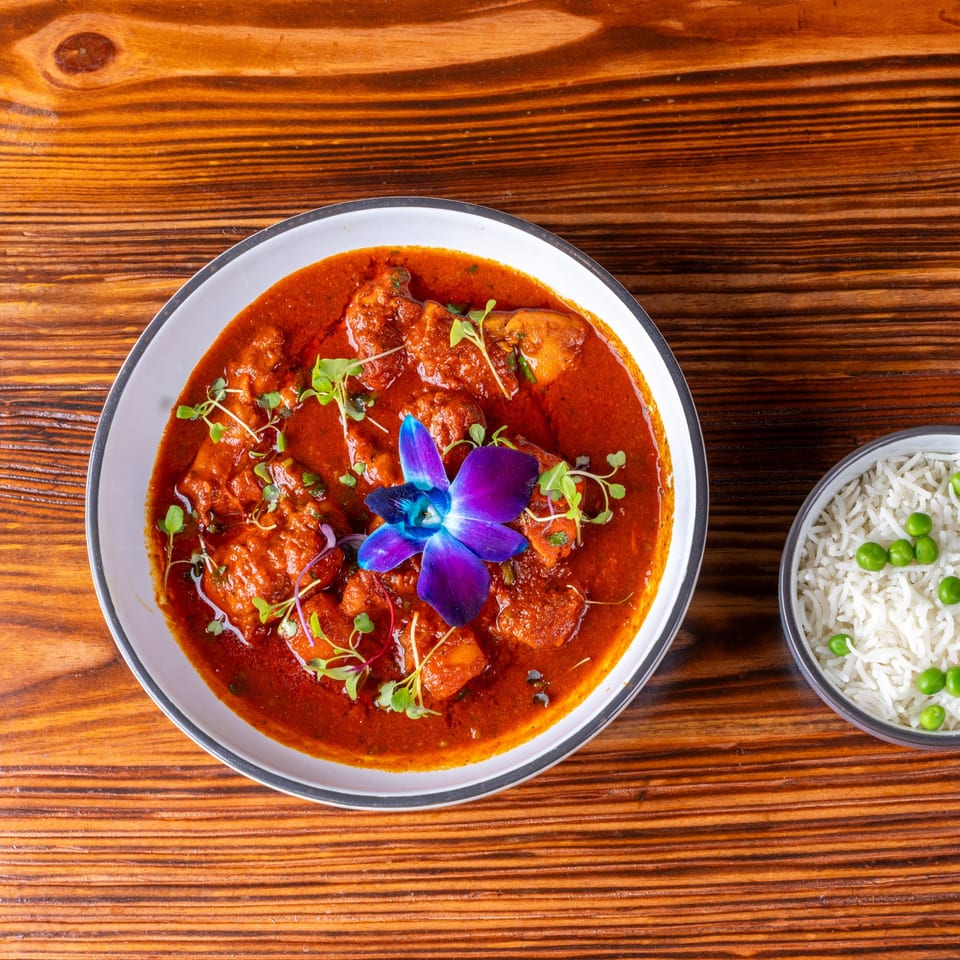 Chicken curry with a purple orchid and microgreens, served with a side of rice and peas.