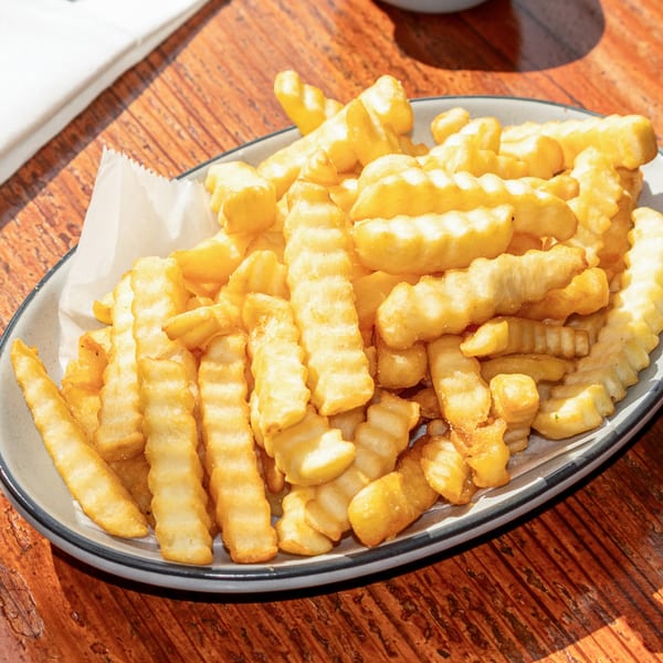 A white plate filled with golden, crinkle-cut french fries sits on a rustic wooden table.