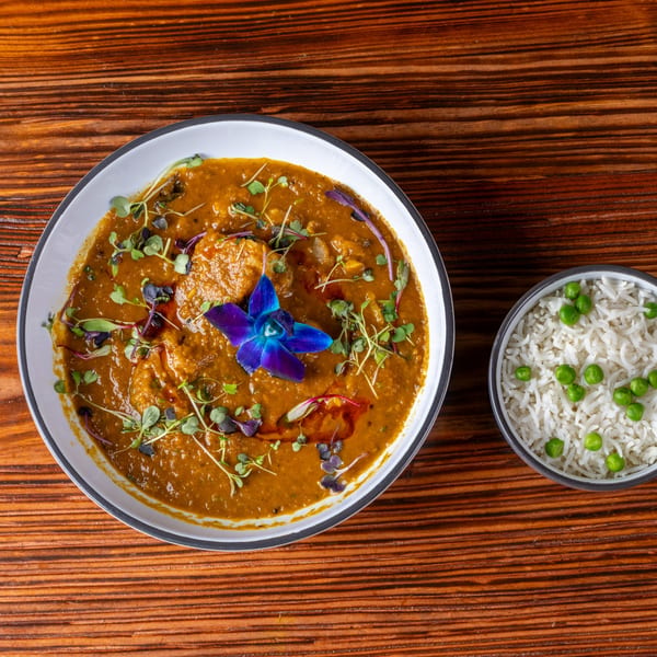 Indian curry with a blue orchid garnish and a side of rice with green peas.
