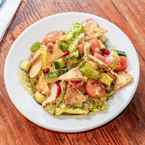 A vibrant fattoush salad with lettuce, tomatoes, cucumbers, radishes, pomegranate seeds, and pita chips.