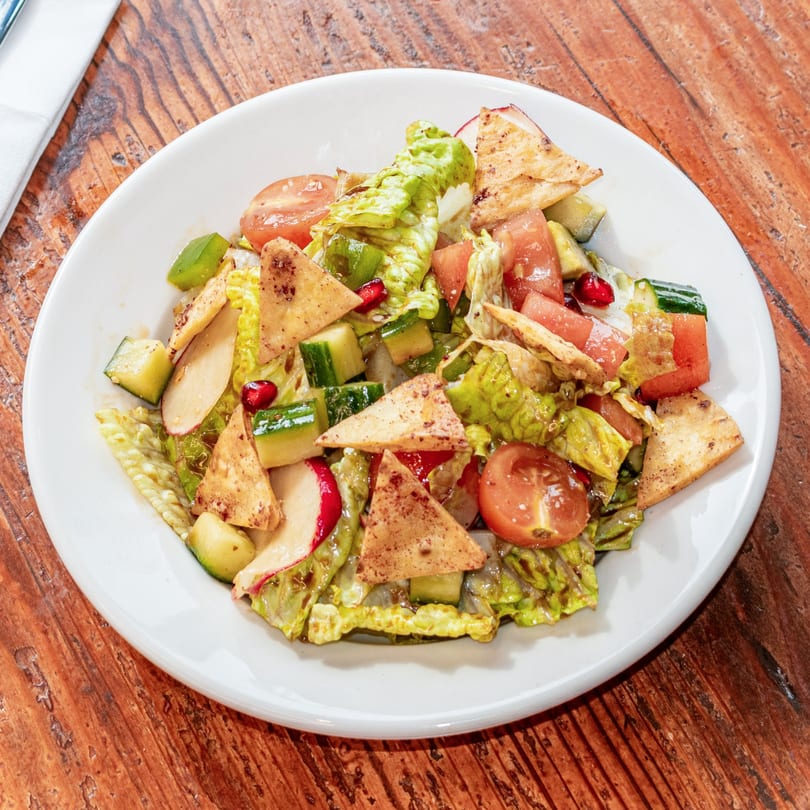 A vibrant fattoush salad with lettuce, tomatoes, cucumbers, radishes, pomegranate seeds, and pita chips.