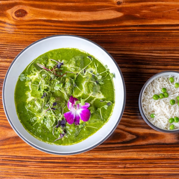 Green curry with a purple orchid garnish, served with a side of rice and green peas.