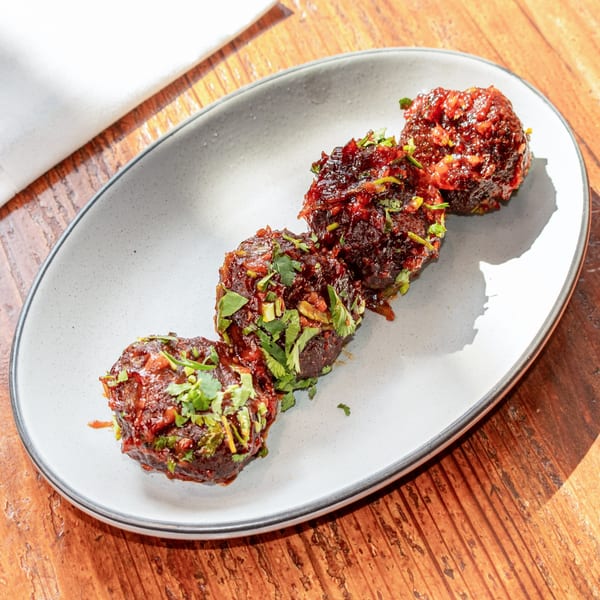 Four dark brown meatballs covered in red sauce and green herbs on a white oval plate.