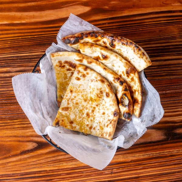 A basket of golden-brown, charred naan bread slices on a wooden table.