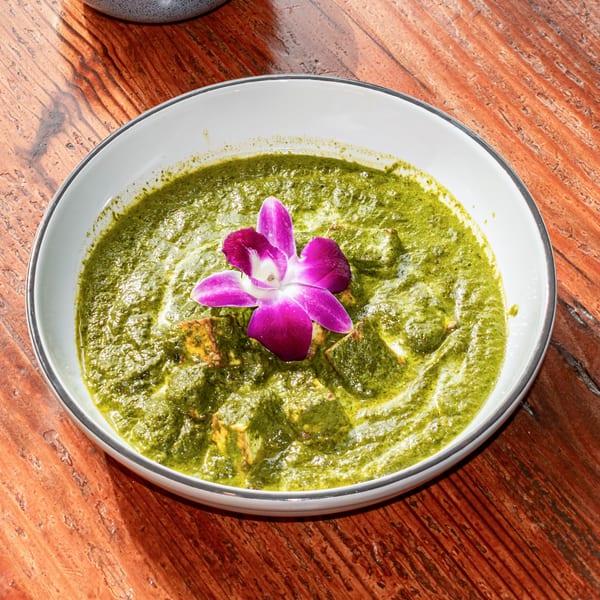Palak Paneer, a green spinach and cheese curry, garnished with a purple orchid on a wooden table.
