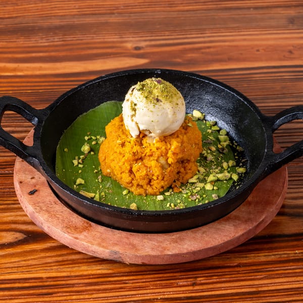 Orange dessert with a scoop of ice cream and pistachios, served in a black skillet on a wooden table.