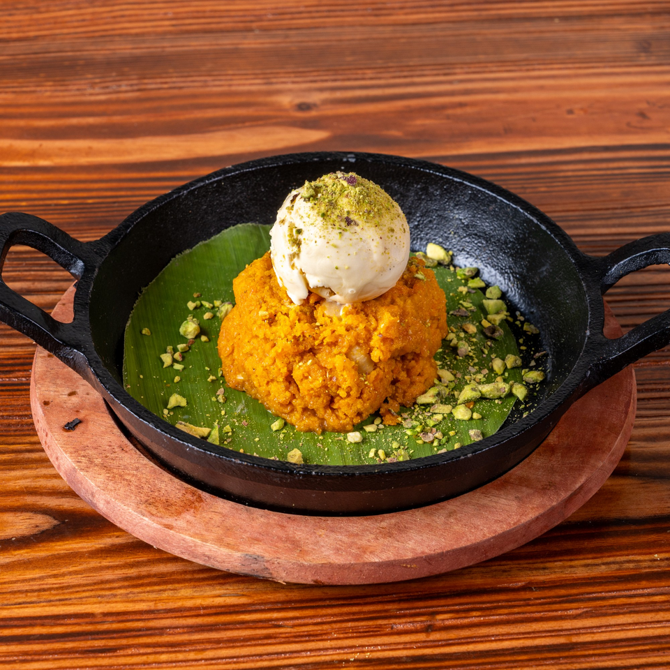 Orange dessert with a scoop of ice cream and pistachios, served in a black skillet on a wooden table.