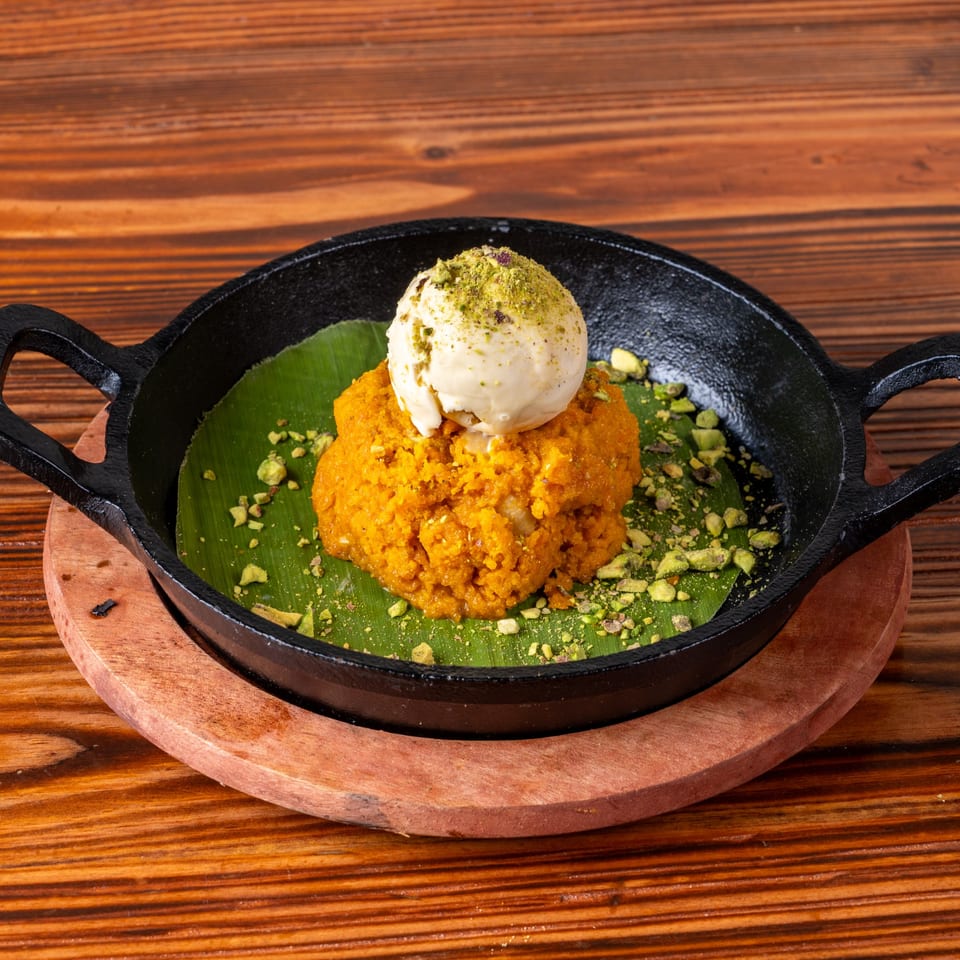 Orange dessert with a scoop of ice cream and pistachios, served in a black skillet on a wooden table.