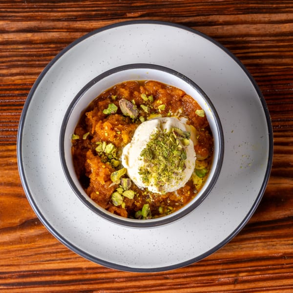 Orange dessert with a scoop of vanilla ice cream and chopped pistachios in a white bowl.