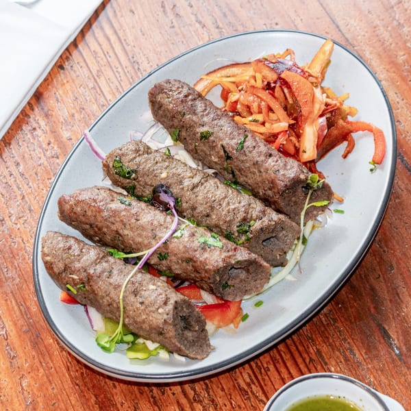 Four seekh kebabs with fresh herbs, served on a bed of salad and pickled vegetables.