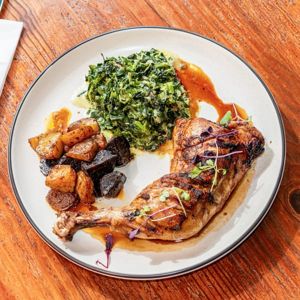 Grilled chicken leg quarter with sautéed greens, roasted potatoes, and beets on a white plate.