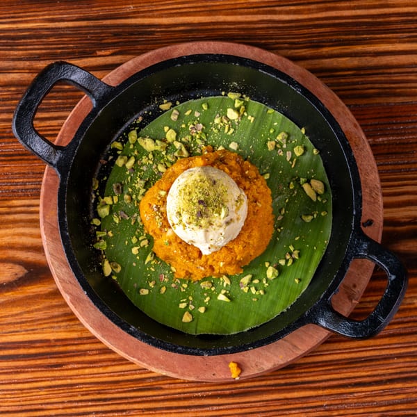 Orange dessert with a scoop of ice cream and pistachios in a black skillet on a wooden table.