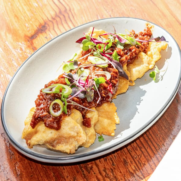 Crispy fried wontons topped with a savory brown sauce, green onions, and microgreens on a white plate.