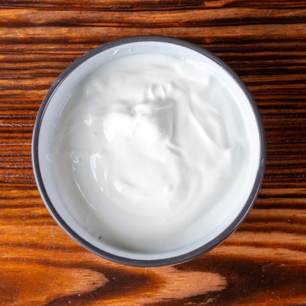 Overhead view of a white bowl filled with creamy white yogurt on a rustic wooden surface.
