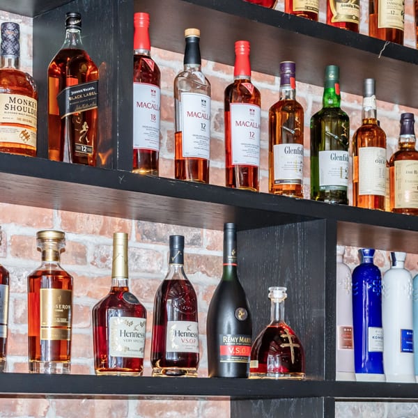 A liquor shelf with various bottles of whiskey, cognac, and other spirits against a brick wall.