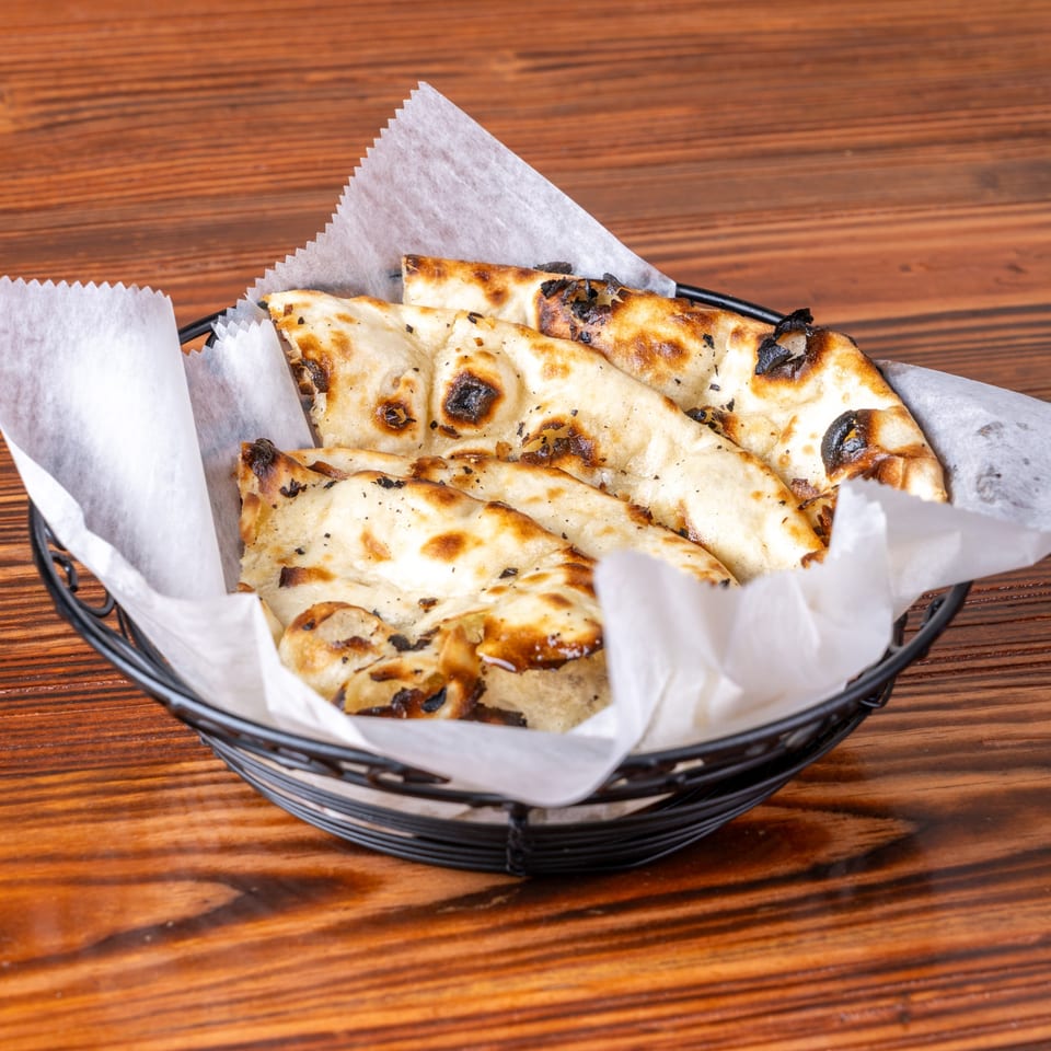 A black wire basket filled with warm, charred naan bread pieces, lined with white parchment paper.