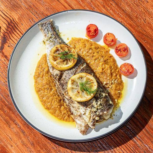Whole roasted fish with lemon slices, dill, and roasted tomatoes on a bed of orange puree.