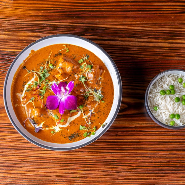 Butter chicken curry with a purple orchid garnish and a side of rice with green peas.