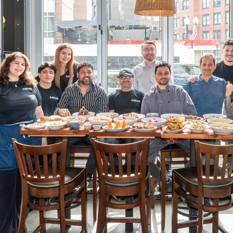 Kahaani restaurant staff and chefs pose with a table full of diverse Indian dishes.