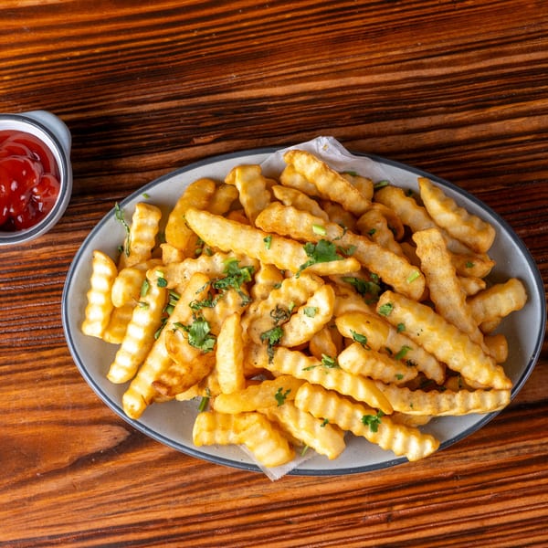 A plate of golden crinkle-cut fries with parsley and a side of ketchup on a wooden table.