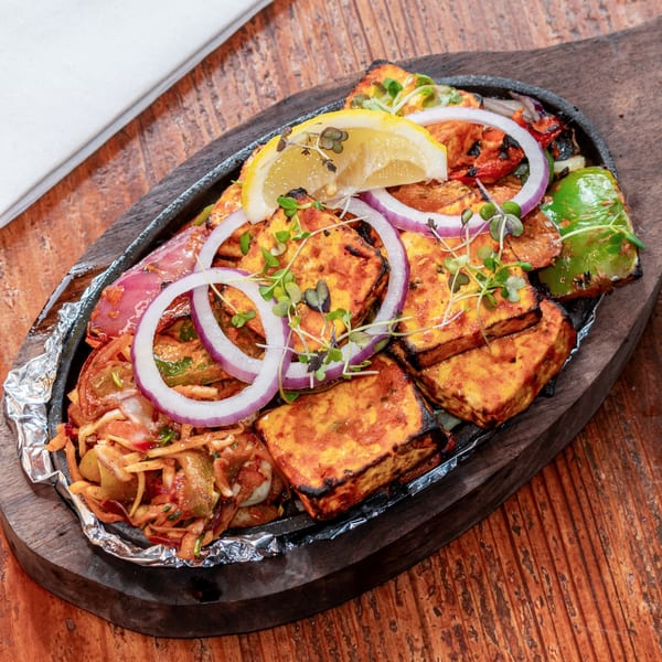 Sizzling paneer tikka with onions, bell peppers, and lemon on a hot plate.