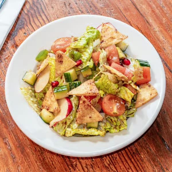 A vibrant fattoush salad with lettuce, tomatoes, cucumbers, radishes, and pita bread on a white plate.