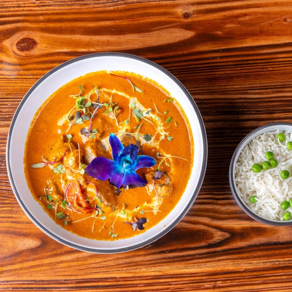 Orange curry with shrimp, microgreens, and a blue orchid, served with a side of rice and peas.