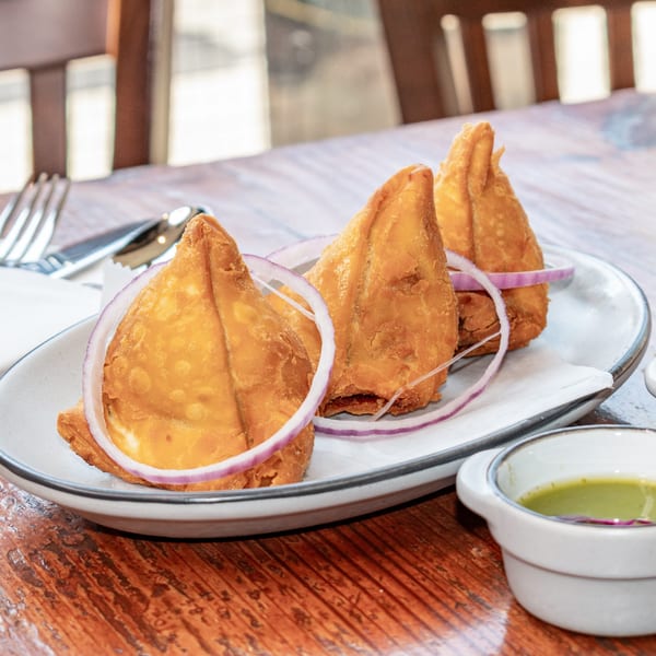 Three golden-brown samosas garnished with red onion rings on a white plate with green chutney.