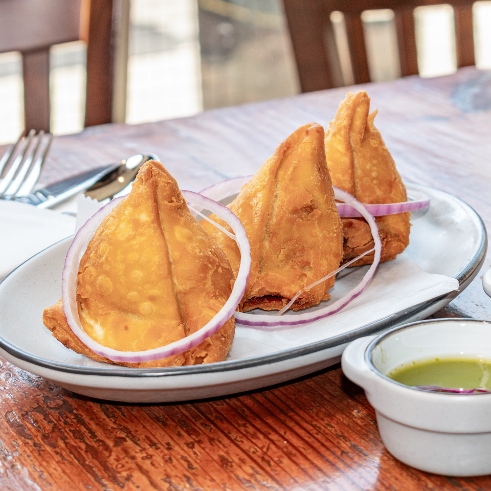 Three golden-brown samosas garnished with red onion rings on a white plate with green chutney.